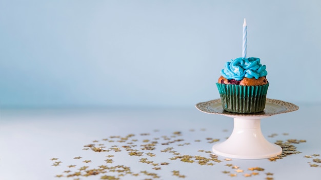 Vela no queque sobre o cakestand contra o fundo azul