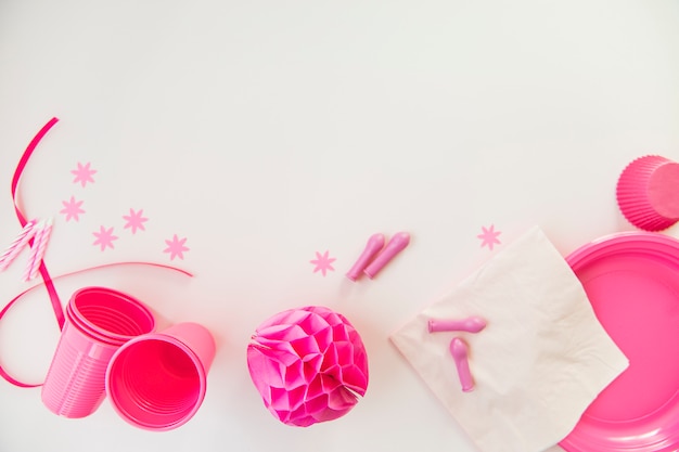 Foto grátis velas cor-de-rosa; copos de plástico; lenco de papel; placas e bola de papel de favo de mel no fundo branco