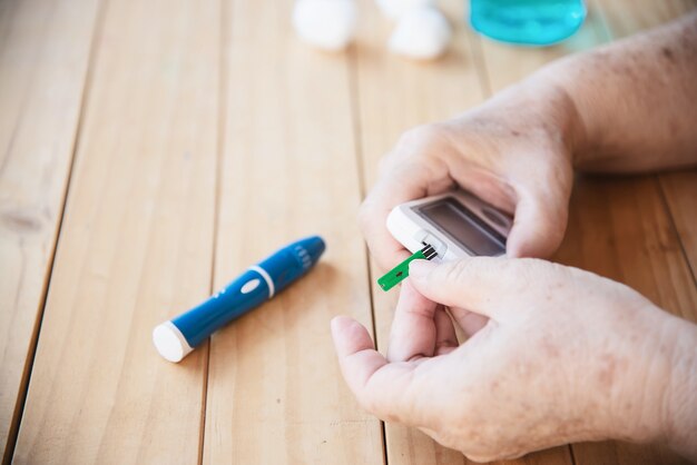 Velha senhora está testando o nível de açúcar no sangue usando o conjunto de criança de teste de açúcar no sangue