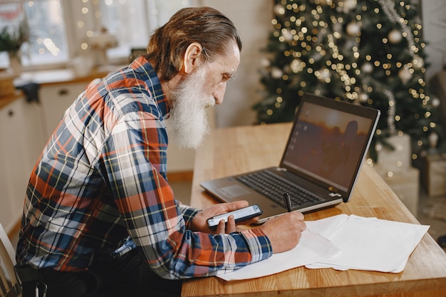 Velho com laptop. avô sentado em uma decoração de natal. homem com telefone celular.