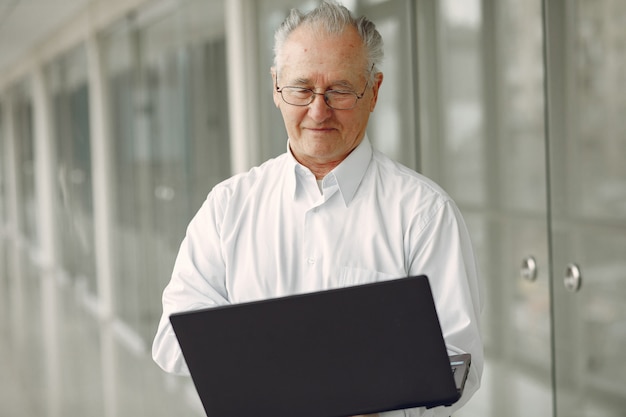 Velho em pé no escritório com um laptop