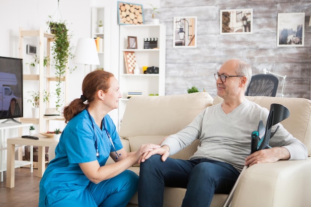 Velho feliz com muletas sentado no sofá no lar de idosos conversando com a médica.