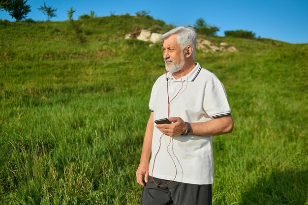 Velho mantendo celular em pé no campo olhando para o lado