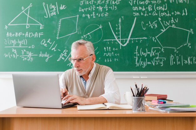 Velho professor usando laptop em sala de aula