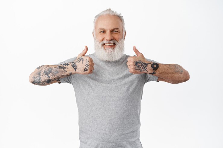 Foto grátis velho sorridente mostra o polegar para cima e parece feliz e orgulhoso, elogia o ótimo trabalho, excelente trabalho, parado satisfeito e satisfeito contra a parede branca