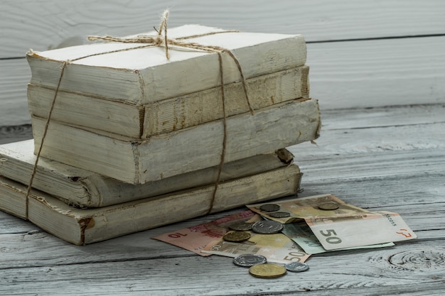 Velhos livros brancos com dinheiro e moedas na parede de madeira