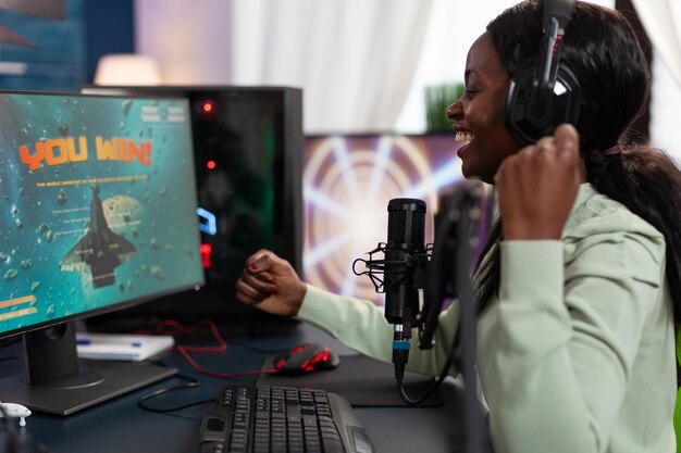 Vencedor de mulher cibernética feliz sentado na mesa de jogos jogando videogames esport ganhando campeonato online. Jogador profissional de sucesso transmitindo ao vivo usando equipamentos de computador RGB. entretenimento lazer