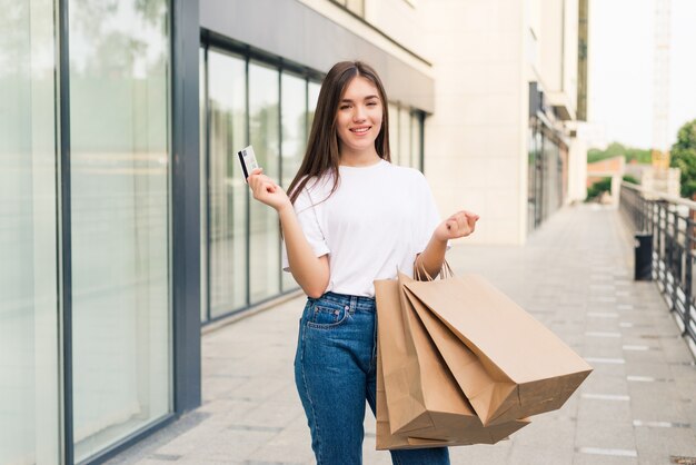 Venda e turismo, conceito de pessoas felizes - linda mulher segurando um cartão de crédito com sacolas de compras na cidade
