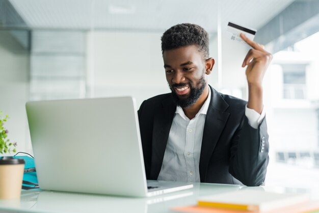 Vendas bancárias na Internet. Empresário africano bem sucedido, sentado em um laptop e segurando o cartão de crédito na mão até o empresário fazer pedidos pela Internet