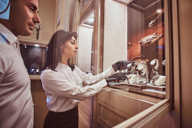 Vendedor mostra ao cliente um relógio masculino exclusivo ao lado de uma vitrine aberta na joalheria de luxo