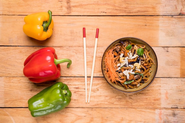 Vermelho; pimentão amarelo e verde com pauzinhos e macarrão udon na mesa