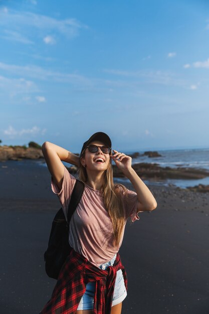 Vertical de mulher viajante feliz olhando para o pé do sol na areia vulcânica preta.