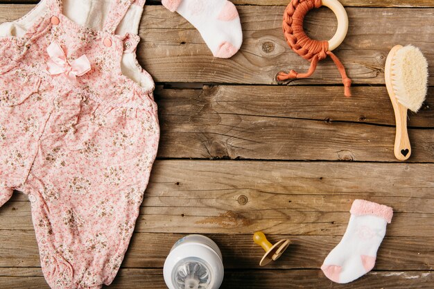 Vestido de bebê; escova; chupeta; brinquedo; meias e garrafa de leite na mesa de madeira