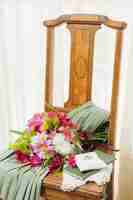 Foto grátis vestido de casamento; bíblia; buquê de flores e anéis de casamento na cadeira de madeira perto da cortina