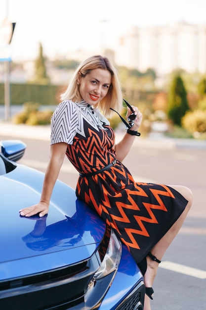 Foto grátis vestido de mulher jovem e deslumbrante posando na frente de seu carro ao ar livre, motorista de propriedade