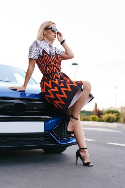 Foto grátis vestido de mulher jovem e deslumbrante posando na frente de seu carro ao ar livre, motorista de propriedade