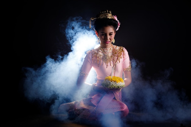 Vestido loykrathong de traje tradicional tailandês ou vestido de ouro do sudeste asiático em mulher asiática com suporte de decoração expressa um sorriso feliz para o festival flutuante loy krathong sobre fundo preto