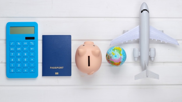 Viagem ou emigração. passaporte com cofrinho, calculadora, globo e avião na superfície de madeira branca. vista do topo. postura plana
