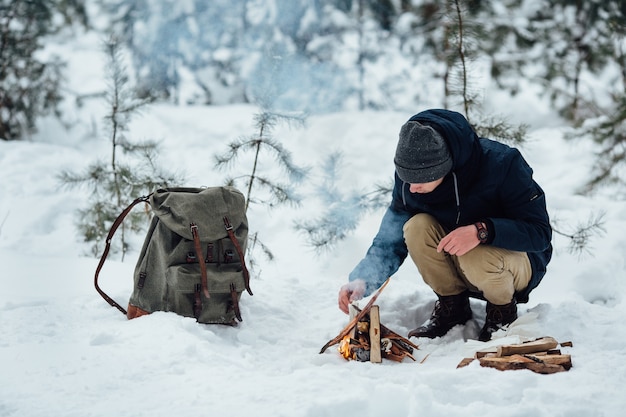 Viajante jovem acende um fogo que esquenta na floresta de inverno