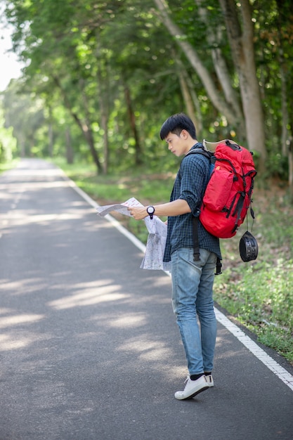 Viajante jovem mochileiro com mapa, ele carrega uma grande mochila durante o relaxamento ao ar livre nas férias de verão no teste da floresta, copie o espaço