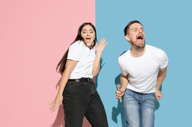 Vibrações. Dançar, cantar, se divertir. Jovem e feliz homem e mulher em roupas casuais na parede bicolor rosa, azul. Conceito de emoções humanas, expressão facial, relações, anúncio. Casal bonito.