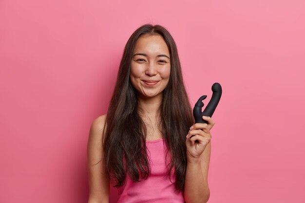 Vida sexual, conceito de masturbação. Mulher sorridente se sente feliz depois de visitar o sex shop, posa com um dispositivo a bateria, segura o vibrador para usar internamente na vagina ou ânus. Maneira fácil de chegar ao clímax
