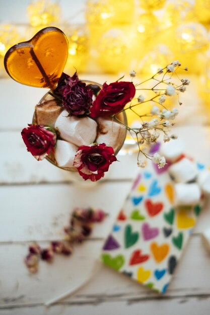 Vidro com café com livro de marshmallow de pirulito de coração de flor rosa seca sobre fundo claro