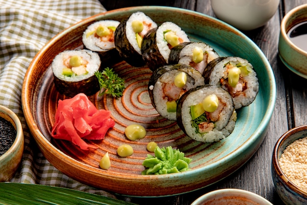 Vie lateral de rolos de sushi com camarão tempura abacate e creme de queijo em um prato com gengibre e wasabi