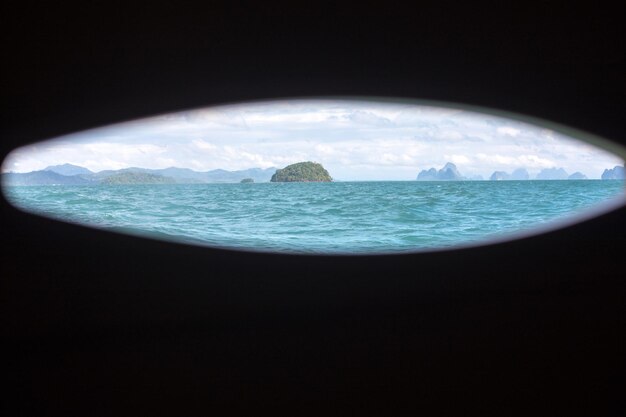 Vigia de barco, vista de barco a vela, o céu azul do oceano e as ilhas verdes e o horizonte [ilustração da foto]. a foto foi tirada dentro de uma cabine em um cruzeiro andaman