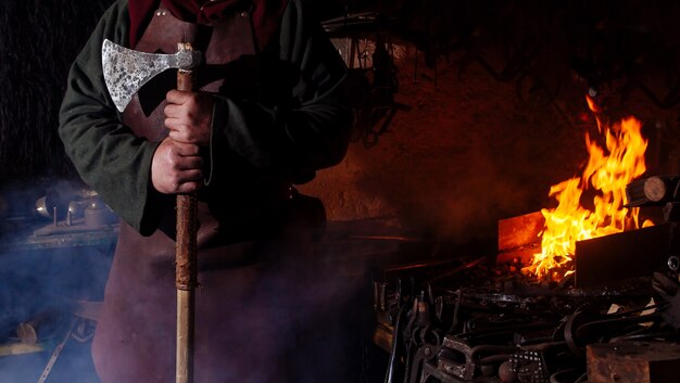Viking forja armas e espadas na ferraria. Um homem com roupas de guerreiro está na ferraria.