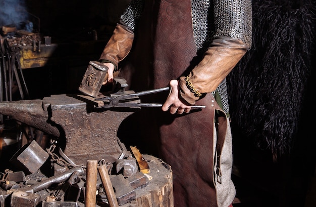Viking forja armas e espadas na ferraria. Um homem com roupas de guerreiro está na ferraria.