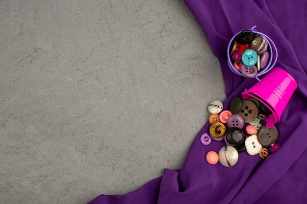 Vintage colorido de botões de plástico dentro de vasos roxos e rosa em um tecido roxo e mesa cinza