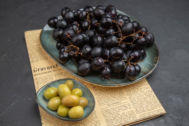 Visão aérea de azeitonas verdes orgânicas frescas e maços de uva preta em um jornal velho em um fundo escuro