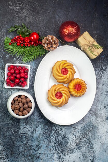 Visão aérea de biscoitos deliciosos em um prato branco e cornel de presente de decorações de ano novo em uma pequena panela de chocolate na superfície escura