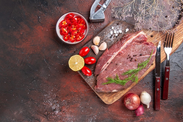 Visão aérea de carne vermelha em uma tábua de madeira e alho verde limão cebola garfo e faca em fundo escuro