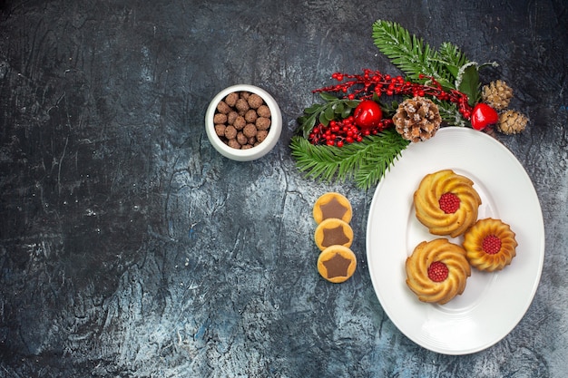 Visão aérea de deliciosos biscoitos em um prato branco, chapéu de Papai Noel e chocolate em uma tigela na superfície escura