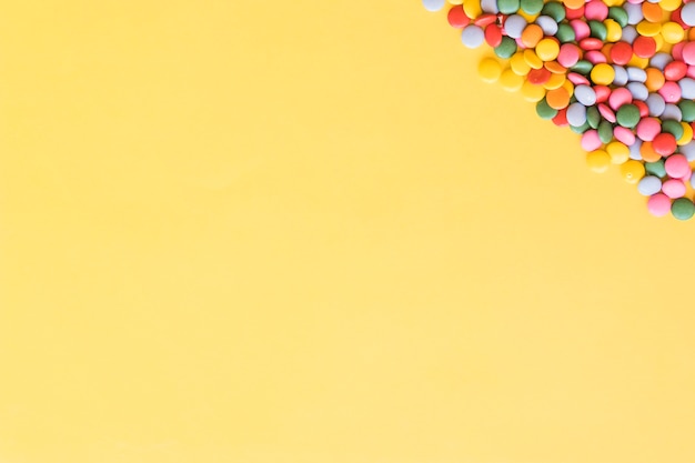 Visão aérea de doces de gemas coloridas no canto do fundo amarelo