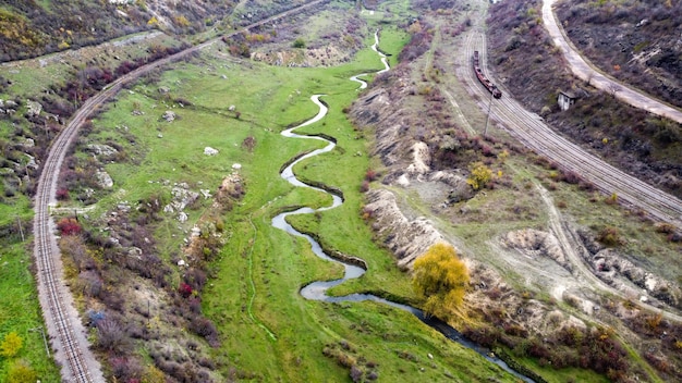 Visão aérea de drones da natureza na Moldávia, fluxo do riacho que flui para a ravina, encostas com vegetação esparsa e rochas, trem em movimento, céu nublado