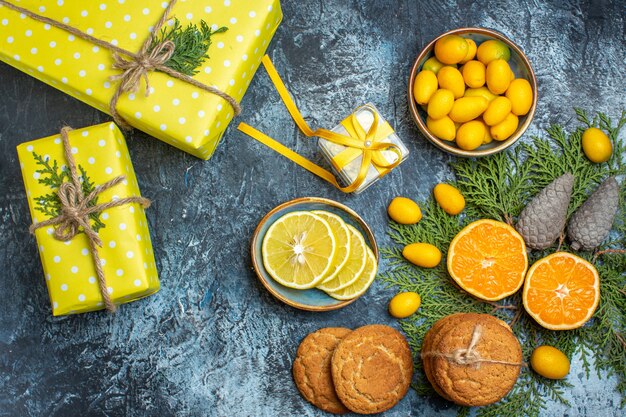 Visão aérea de frutas cítricas frescas e inteiras e biscoitos de coníferas em caixa de presente amarela em fundo escuro