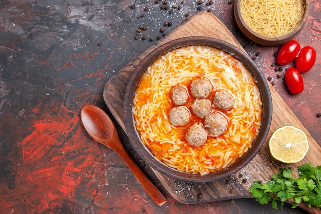 Visão aérea de saborosa sopa de almôndegas com macarrão a bordo de macarrão de madeira de limão um monte de verduras na mesa escura