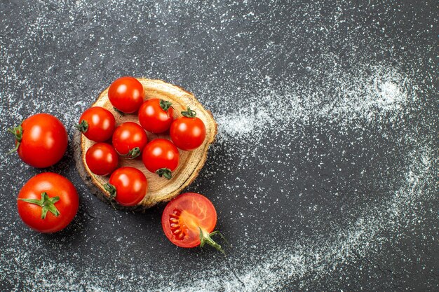 Visão aérea de tomates frescos com caules na placa de madeira do lado direito sobre fundo branco e preto