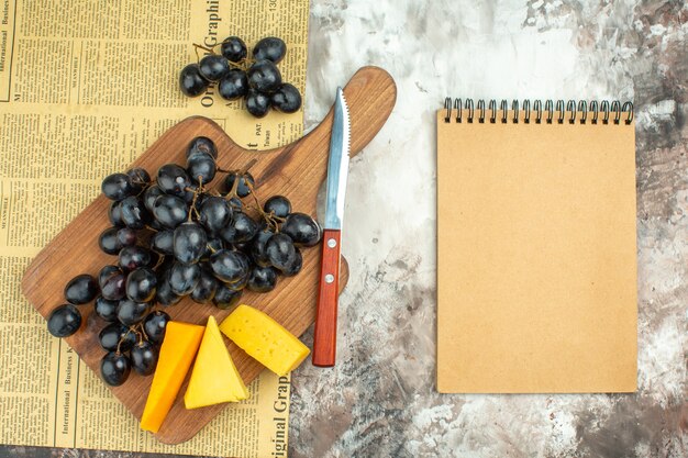 Visão aérea de um delicioso cacho de uvas pretas frescas e vários tipos de queijo na tábua de madeira