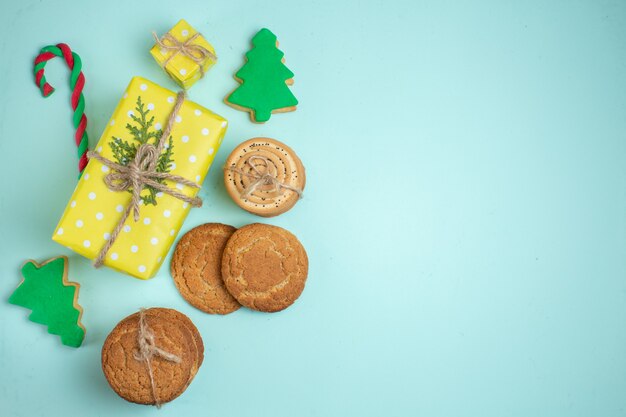 Visão aérea de vários biscoitos de açúcar de árvore de Natal e caixa de presente amarela em fundo azul pastel