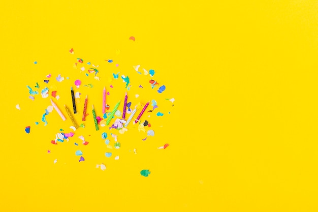 Visão aérea de velas coloridas com confetes em fundo amarelo