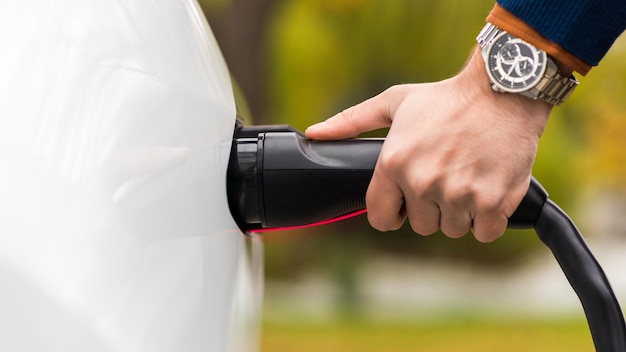 Visão aproximada de um homem conectando o carregador a uma porta de carregamento de carro elétrico