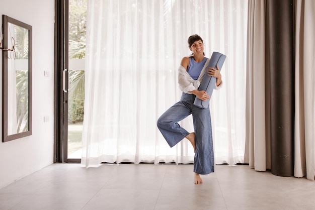 Visão completa da mulher sorridente com tapete de fitness fazendo pose de esporte