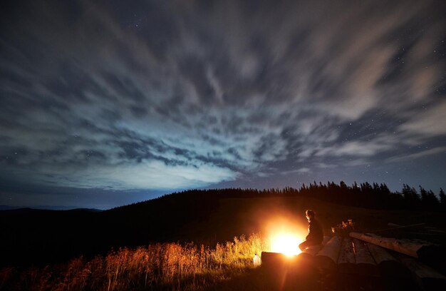 Visão de grande angular na noite estrelada nublada nas montanhas e um homem curtindo a natureza