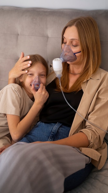 Foto grátis visão de mãe e filha usando nebulizador em casa para problemas de saúde respiratória