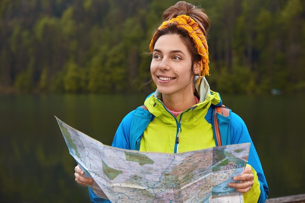 Visão externa horizontal do viajante satisfeito, verifica a rota no mapa de localização e explora um novo lugar