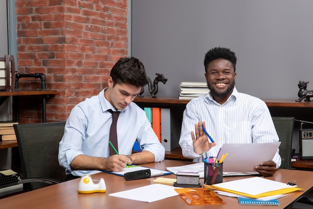 Visão frontal de dois parceiros de negócios trabalhando no escritório, um deles escrevendo algo